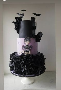 a three tiered cake with black ruffles and a doll on it's side