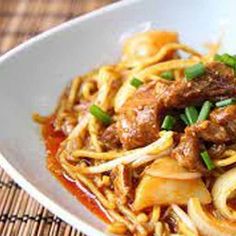 a white bowl filled with noodles and meat on top of a bamboo place mat next to a fork