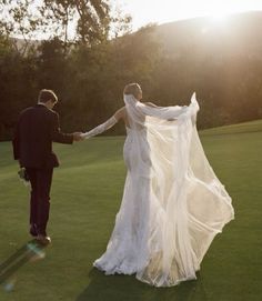 a bride and groom holding hands while walking through the grass