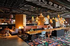 an empty restaurant with many chairs and lights hanging from the ceiling, along with colorful rugs