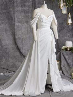 a white wedding dress on display in front of a gray backdrop with candles and flowers