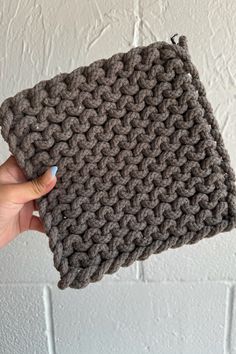 a hand holding up a gray crocheted pouch on top of a white wall