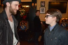 two young men standing next to each other in front of a christmas tree at a bar