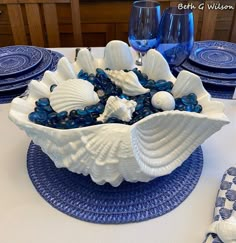 a blue and white place setting on a table with plates, wine glasses and napkins