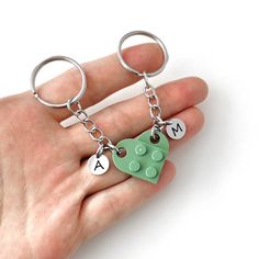 a hand holding two key chains with letters and a lego piece attached to the chain