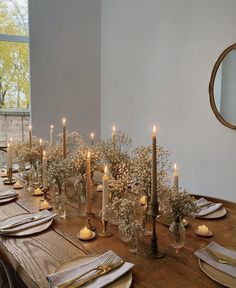 a long table with candles and place settings on it in front of a large window