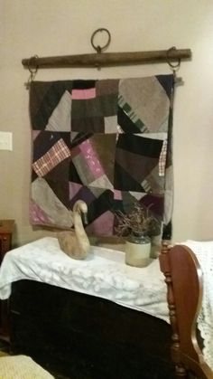 a bed with a quilt hanging on the wall and a potted plant in front of it