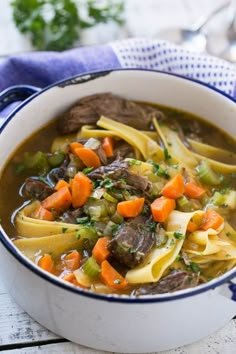 a white bowl filled with beef and pasta soup on top of a blue and white checkered napkin