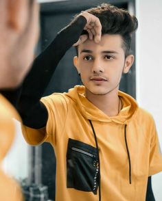 a young man in a yellow hoodie is looking at his reflection in the mirror