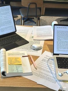 two laptops sitting on top of a wooden table next to books and headphones