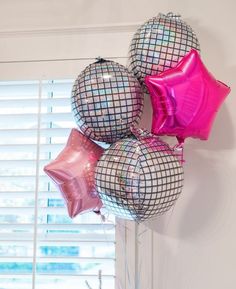 some pink and silver balloons are hanging on the wall in front of a window with shutters