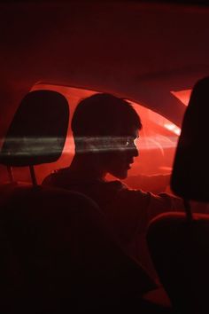 a man sitting in the passenger seat of a car with red light coming from behind him