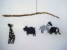 three black and white paper cut animals hanging from a tree branch, with one giraffe in the background