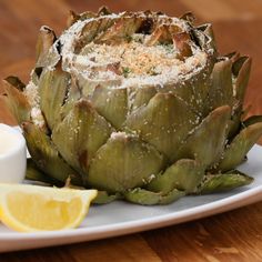 an artichoke on a white plate with lemon wedges and salt next to it