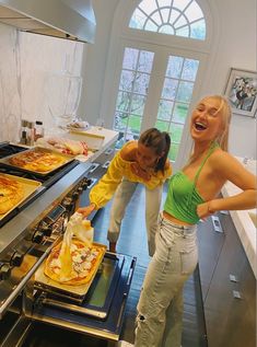 two women standing in front of some pizzas