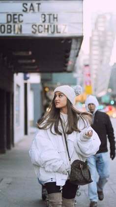 a woman is walking down the street with her hand in her pocket and wearing a white jacket