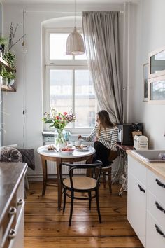 a woman sitting at a table in front of a window with flowers on the windowsill