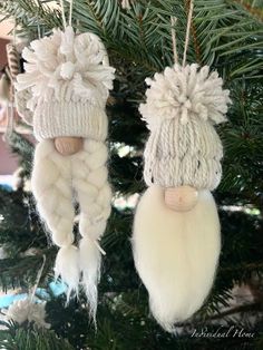 two white knitted hats hanging from a christmas tree with pom - poms