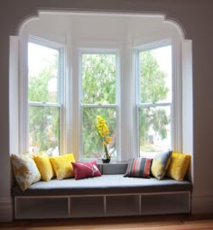 a window seat with yellow and red pillows on it in front of a bay window