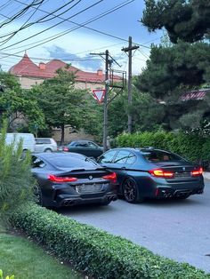 two cars parked side by side on the street next to some bushes and trees with power lines above them