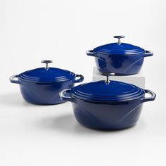 three blue casserole dishes with lids and handles on a white background, set against a plain backdrop