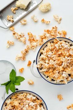 two bowls filled with popcorn next to a grater and scooper on a white surface