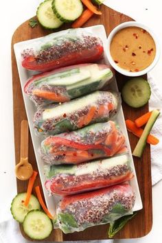 several vegetables wrapped in plastic sitting on a cutting board next to some dipping sauces