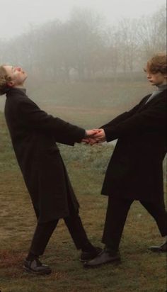 two people holding hands in the middle of a foggy field with trees in the background