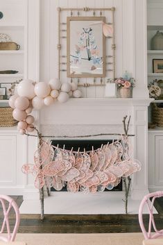 pink and white balloons are hanging from the mantle in front of a fireplace with chairs