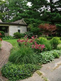 a brick walkway in front of a house surrounded by flowers and greenery on the side