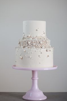 a three tiered white wedding cake on a pink stand