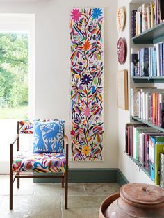 a wooden chair sitting in front of a book shelf next to a large painting on the wall