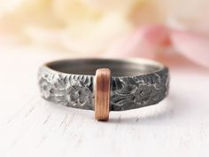 a close up of a ring on a white surface with flowers in the back ground