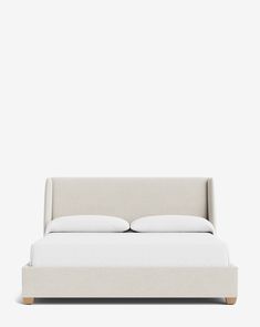 a bed with white sheets and pillows on it's headboard, in front of a gray wall