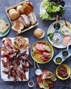 a table topped with plates and bowls filled with different types of food next to buns