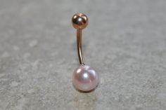 a gold nose piercing with a pink pearl on it's end, sitting on a gray surface