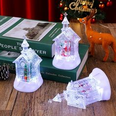 two christmas lights sitting on top of green books next to a small house and tree