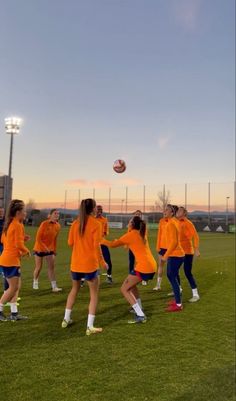 girls in orange shirts playing soccer on a field at sunset with the sun setting behind them