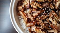 a white bowl filled with rice covered in sesame seeds and sliced meat on top of it