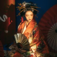 a geisha sitting on the ground with an umbrella in her hand and holding a fan