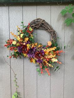 a wreath hanging on the side of a building with flowers and greenery around it