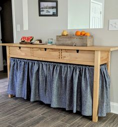 a wooden table topped with fruit on top of a hard wood floor covered in blue ruffles