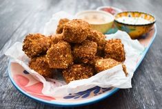 a plate full of fried food with dipping sauces on the side and another bowl in the background