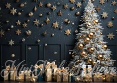 a christmas tree with gold and silver presents in front of a wall decorated with stars