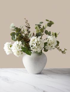 a white vase filled with flowers on top of a marble counter topped with greenery