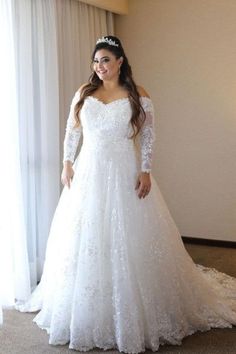 a woman in a white wedding dress standing next to a window wearing a tiara