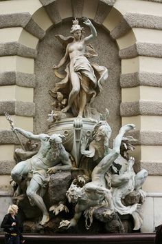 a statue on the side of a building with many statues around it and an arch in the background