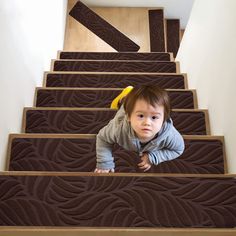 a toddler crawling down some stairs with his head on the handrail and looking at the camera