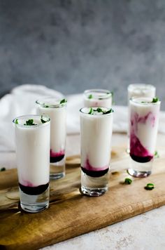 four glasses filled with liquid sitting on top of a wooden board