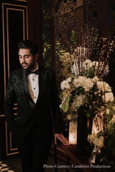 a man in a tuxedo standing next to a flower arrangement